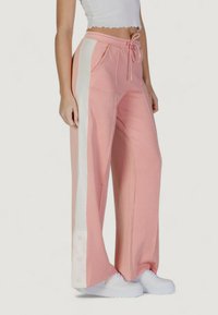 Pantaloni a gamba larga rosa con strisce bianche laterali, dotati di una vita con cordoncino e tasche, realizzati in un tessuto morbido. Dettaglio di bottone significativo all'orlo.