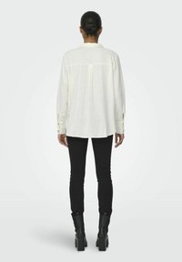 Weiße Langarmbluse mit Rückenpasse und geknöpften Manschetten, kombiniert mit schwarzen engen Jeans und Stiefeletten mit Absatz. Weicher, leichter Stoff.