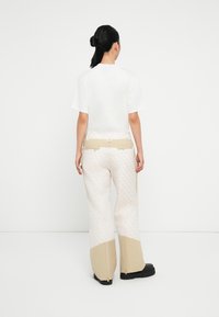 T-shirt blanc associé à un pantalon beige à motifs avec une coupe large, des zips aux chevilles et un détail de ceinture contrastant.
