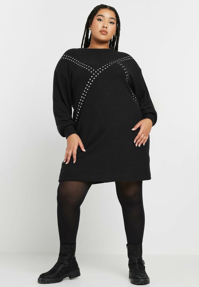 Abito nero a maglia con maniche lunghe, caratterizzato da un motivo a incrocio di borchie argentate. L'abito ha una vestibilità ampia e arriva a metà coscia.