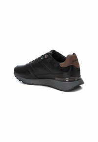 Scarpa sportiva nera con superiore texture, accenti in scamosciato, colletto imbottito e suola in gomma. Presenta loghi a contrasto e occhielli metallici.