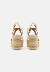 Sandali espadrillas beige con forma arrotondata, dotati di un tacco spesso intrecciato e due cinturini regolabili con una fibbia dorata.