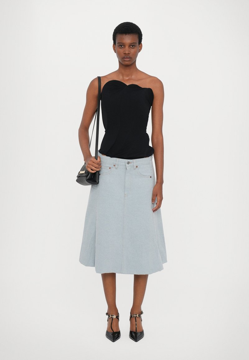 Schwarzes Top mit einem Schulterträger, figurbetontes Design. Hellblauer Denim-A-Linien-Rock, knielang, mit Vorderknöpfen. Schwarze spitze Absätze und kleine Tasche.