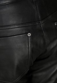 Zwarte leren broek met een gladde textuur, zichtbare stiksels en een klassiek zakontwerp met metallic accenten.