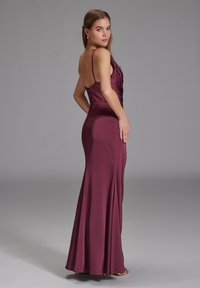 Lang, tætsiddende kjole i burgunderrød satin med tynde spaghetti-stropper og en draperet døgn design, der har en subtil sideslids og en glat tekstur.