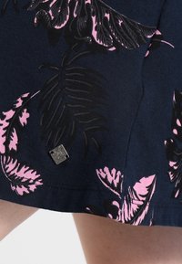 Blommig kjol med svarta och rosa bladmönster på en marinblå bakgrund. Inkluderar en liten silverfärgad märkesetikett vid fållen.