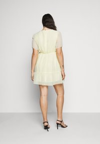 Abito giallo chiaro a maniche corte con orlo a strati, realizzato in tessuto trasparente con texture a pois, con vita elasticizzata e chiusura a bottone sul retro.