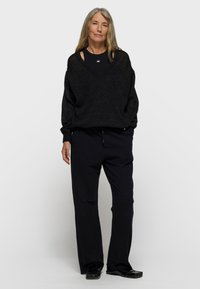 Zwarte oversized trui met een V-hals en verlaagde schouders, gecombineerd met losvallende zwarte broek. Genuanceerd gebreid materiaal met een subtiele glans.