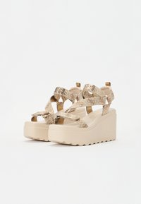 Beige Keilsandalen mit gemusterten Stoffriemen, verstellbaren Schnallen und einer klobigen Plattformsohle. Texturierte Gummisohle für besseren Halt.