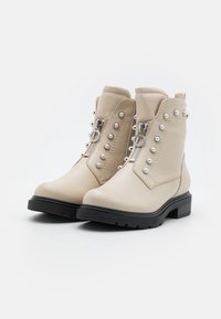 Beige leather ankle boots with a zip closure, decorative silver studs, textured design, and black rubber sole.