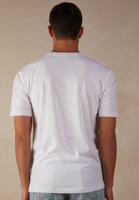 T-shirt en coton blanc à manches courtes et col rond. Texture lisse, coupe ajustée et design simple sans motifs ou accents visibles.