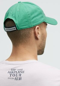 Green cotton baseball cap with a curved brim, featuring a navy and white striped adjustable strap at the back. Simple, classic design.