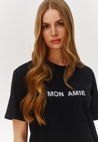 Czarny t-shirt z krótkim rękawem z napisem "MON AMIE" w kontrastowych białych literach blokowych. Gładki bawełniany materiał o luźnym kroju.
