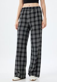 Pantalons larges à carreaux noir et blanc avec une taille élastique, fabriqués dans un tissu léger. Présente une coupe décontractée et un design fluide.