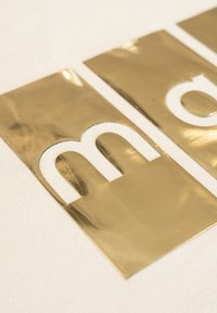 Złote metaliczne litery tworzące "m" i "o" na białej teksturowanej powierzchni. Litery mają gładkie wykończenie i ostre krawędzie.