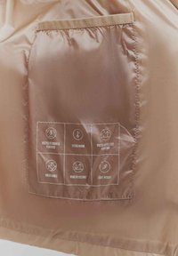 Brown jacket interior featuring a stitched pocket with icons indicating features: recycled down, warmth, water repellency, breathability, wind resistance, light weight.
