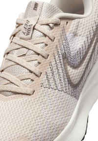 Scarpa atletica beige chiaro con tomaia in mesh traspirante, dettagli testurizzati e suola bianca. Presenta il logo Nike swoosh grigio.