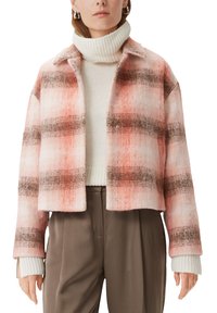 Różowo-pomarańczowa kratkowana kurtka typu cropped o miękkiej fakturze, z brązowymi paskami i srebrnymi zatrzaskami, noszona na białym golfie.