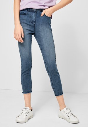 Blauwe spijkerbroek met een hoge taille en een korte lengte, met een rafelige zoom, voorszakken en subtiele stiksel details. Gecombineerd met witte sneakers.