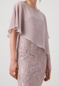 Robe rose clair avec une couche supérieure fluide et transparente et un bas en dentelle à sequins, ornée de motifs floraux et d'une coupe ajustée.