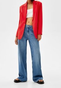 Punainen bleiseri valkoisen lyhyen topin päällä, yhdistetty vaaleansinisiin leveälahkeisiin farkkuihin. Asussa on sileä kangas ja siistit linjat. Mustat korolliset sandaalit.