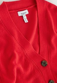 Red cardigan made of soft fabric featuring a deep V-neck, two large dark buttons, and subtle textured lines along the front. Size S tag visible.