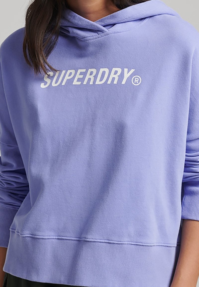 Sweat à capuche violet clair en tissu doux, avec une capuche à cordon de serrage et un logo blanc "SUPERDRY" sur la poitrine. Poignets et ourlet côtelés.