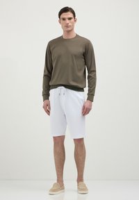 Maglietta a maniche lunghe verde oliva, pantaloni corti bianchi con coulisse e scarpe beige senza lacci. Design semplice con trame lisce e colori neutri.