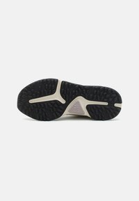 Egy sneaker talpa, amely texturált fekete gumifelülettel, geometrikus mintázatokkal és világos bézs középtalppal rendelkezik, amelyen logó részlet található.