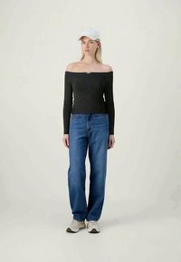 Top negru cu umerii la vedere, cu buline, cu mâneci lungi, purtat cu blugi evazați albaștri cu talie înaltă și pantofi sport de culoare deschisă.