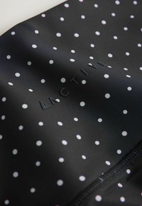 Tissu noir à pois blancs avec le texte en relief "ACTIVE", présentant de légers plis et des coutures le long du bord.