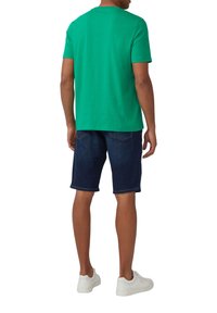 Zielona koszulka bawełniana z okrągłym dekoltem, w połączeniu z ciemnoniebieskimi szortami dżinsowymi i białymi sneakersami, widok z tyłu.