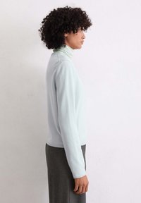 Maglione azzurro chiaro con collo a lupetto in tessuto morbido, con maniche lunghe e design aderente, abbinato a una gonna grigia con texture.