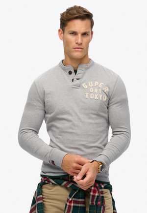Gray long-sleeve pullover with a henley neckline, featuring wooden buttons and "SUPER DRY TOKYO" text. Textured fabric and slim fit design.