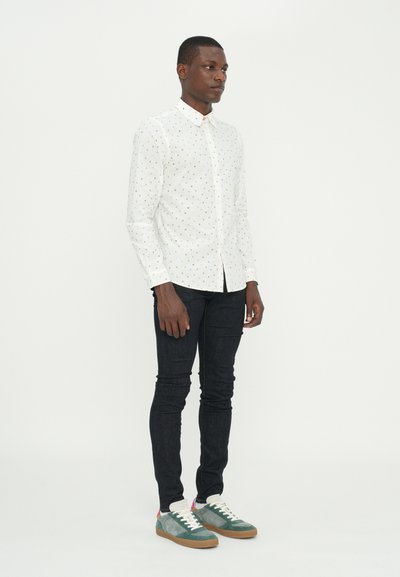 White button-up shirt with multicolored polka dots, paired with slim-fit dark jeans and green sneakers with white laces and tan soles.