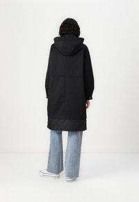 Svart lang frakk med hette, med en quiltet nedre del. Sammen med lyseblå vide jeans og hvite sneakers.