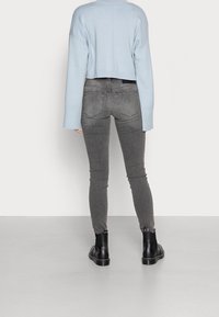 Suéter corto de color azul claro con mangas anchas, combinado con jeans ajustados de color gris oscuro. La modelo lleva botas de tobillo negras con un acabado liso.