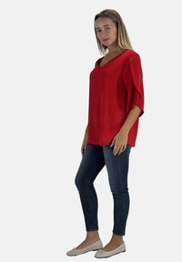 Rode v-hals blouse met korte, brede mouwen; textuurstof; gecombineerd met slim-fit blauwe jeans en beige ballerina's. Eenvoudig, modern ontwerp.