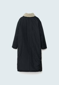 Long manteau noir matelassé avec col en fausse fourrure beige, manches longues et ourlet droit, vu de dos sur un fond gris clair.