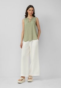 Blouse sans manches vert olive avec détail de col froncé, associée à un pantalon large blanc et des sandales plateformes crème.