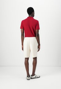 Polo rouge à manches courtes, short crème et baskets noir et blanc. Texture lisse et coupe décontractée, vu de dos.