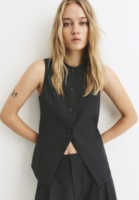 Schwarze Nadelstreifen-Weste mit rundem Ausschnitt und vertikaler Naht, ausgestattet mit sechs vorderen Knöpfen und einem taillierten, kurzen Design.