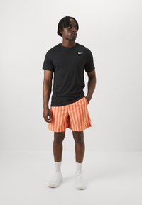 Camiseta negra de Nike, pantalones cortos a rayas naranjas, zapatillas blancas y calcetines cortos blancos. Diseño simple con cuello redondo y mangas cortas.