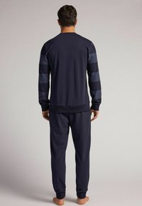 Marineblaues Sweatshirt- und Hosen-Set; das Sweatshirt hat gestreifte marineblaue Ärmel, gerippte Bündchen und einen runden Halsausschnitt; der Stoff scheint weich und strukturiert zu sein.