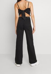 Svart satin crop top med knytning bak, kombinerat med högmidjade svarta vida jeans. Modellen har på sig vita klumpiga sneakers.