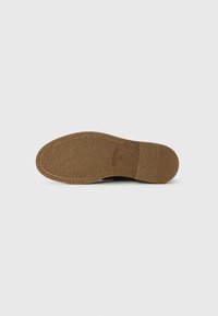 Rubber sole of brown shoe with visible stitching and small textured heel section on plain white background.