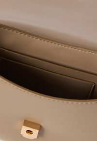 Beżowa skórzana torebka z złotym prostokątnym zapięciem i widoczną otwartą kieszonką wewnątrz.