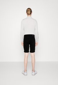Svarte denimshorts med rullekanter, kombinert med en lys grå langermet skjorte og hvite sneakers. Vist fra baksiden.