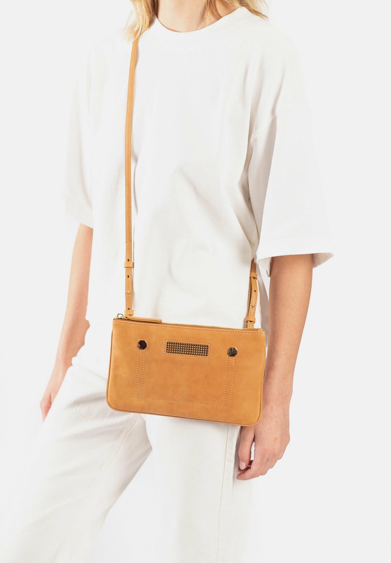 Tan leren crossbody tas met een rechthoekige vorm, ritssluiting, metalen accenten en twee gaten voor het bevestigen van de verstelbare schouderband.