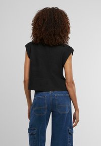 Top senza maniche lavorato a maglia nera con orlo a costine, abbinato a pantaloni cargo in denim blu con ampie tasche e dettagli di cucitura visibili.